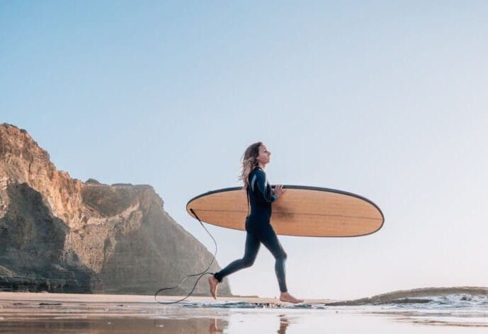 Young woman on beach carries surfboard ready for a surf session